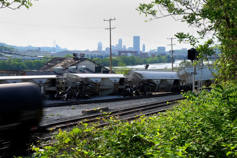 An oil car speeds past a derailed train in the Hazelwood neighborhood of Pittsburgh. Downtown Pittsburgh is less than three miles away. © Brian Cohen, 2015.