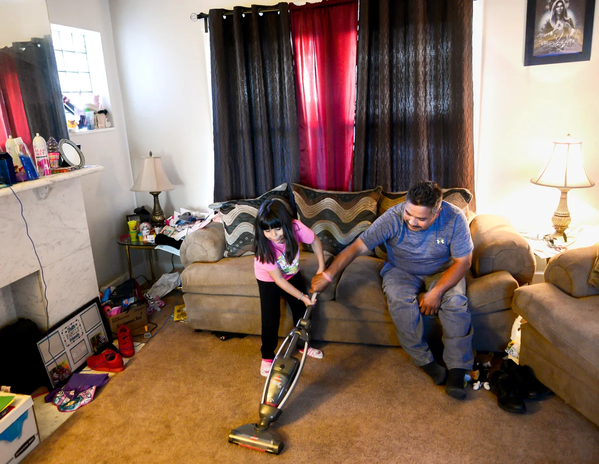 Brianna helps her father Jose vacuum the living-room floor. © Nate Guidry/TDW 2017