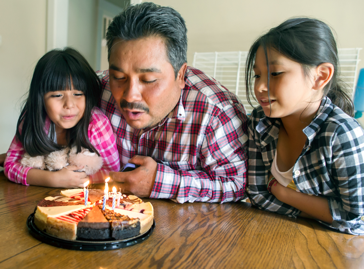  Brianna and Emma look on as Jose blows out candles on a birthday cheesecake. He was celebrating with his daughters and a few friends.  © Nate Guidry/TDW 2017 