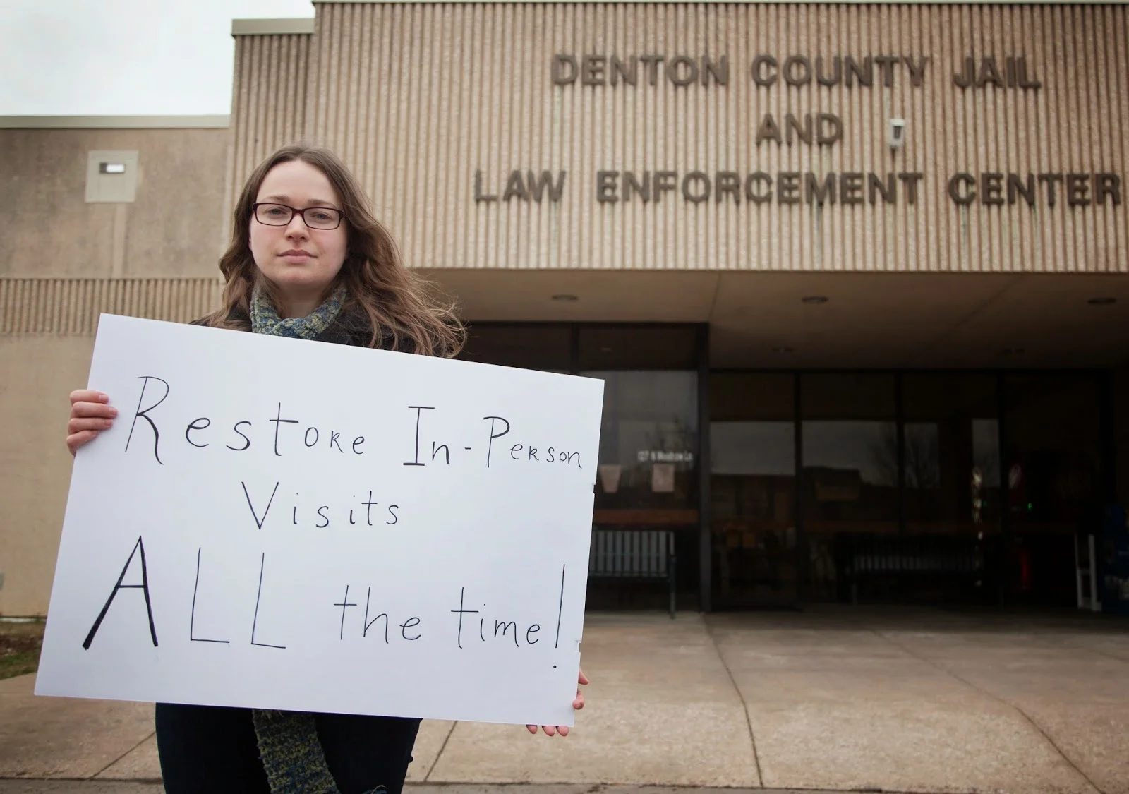 Jennifer Long posed with a sign that reads, "Restore in-person visits all the time!" in front of the Denton County Jail where protesters gathered Feb. 26, 2015, to protest the jail's video visitation system. Photo by Kristen Watson for the Denton Record-Chronicle.