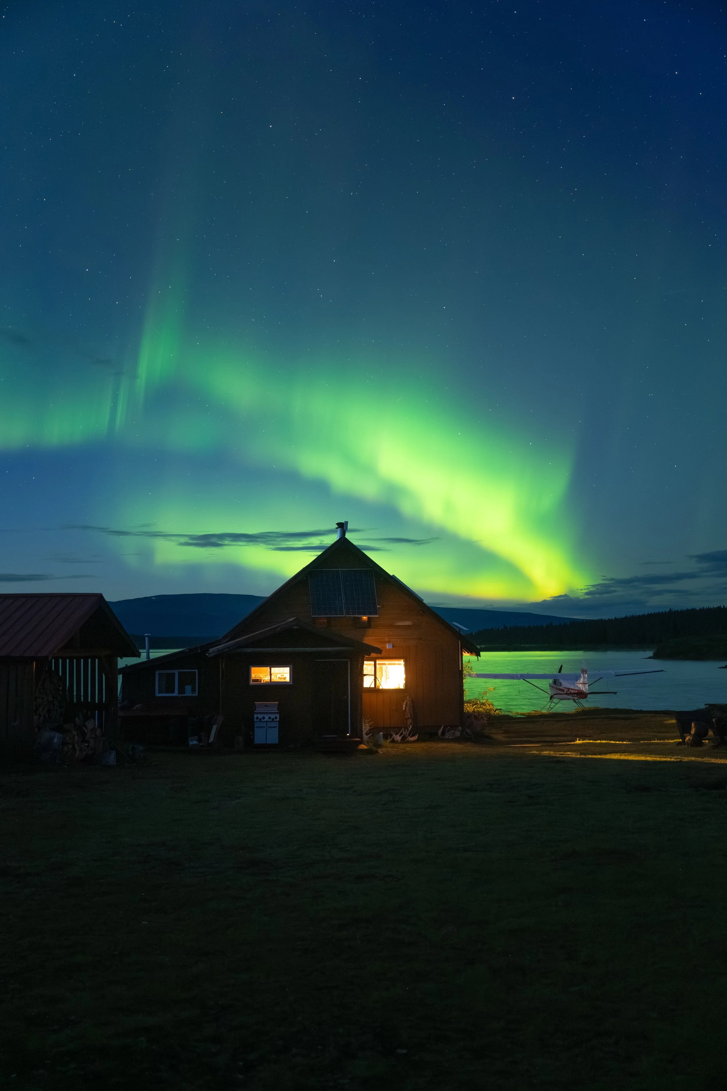 Aurora Borealis Dancing over a lit up cabin at Spatsizi Lodge, on the shore of Laslui Lake in Spatsizi Plateau Wilderness Provincial Park, in Northern British Columbia, Canada.