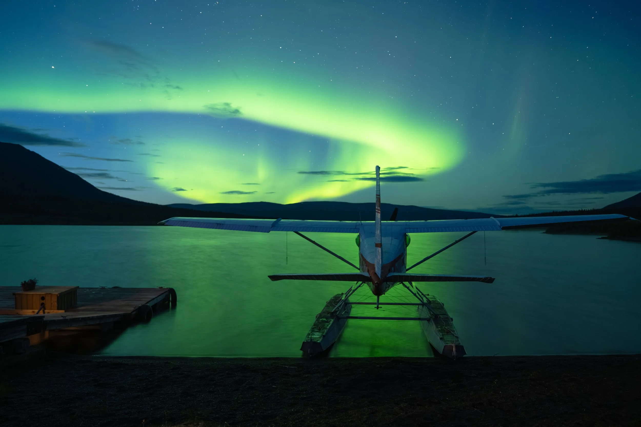 Bright northern lights dancing over Laslui Lake and a Cessna 185 float plane in Spatsizi Plateau Wilderness Provincial Park on a clear summer night.
