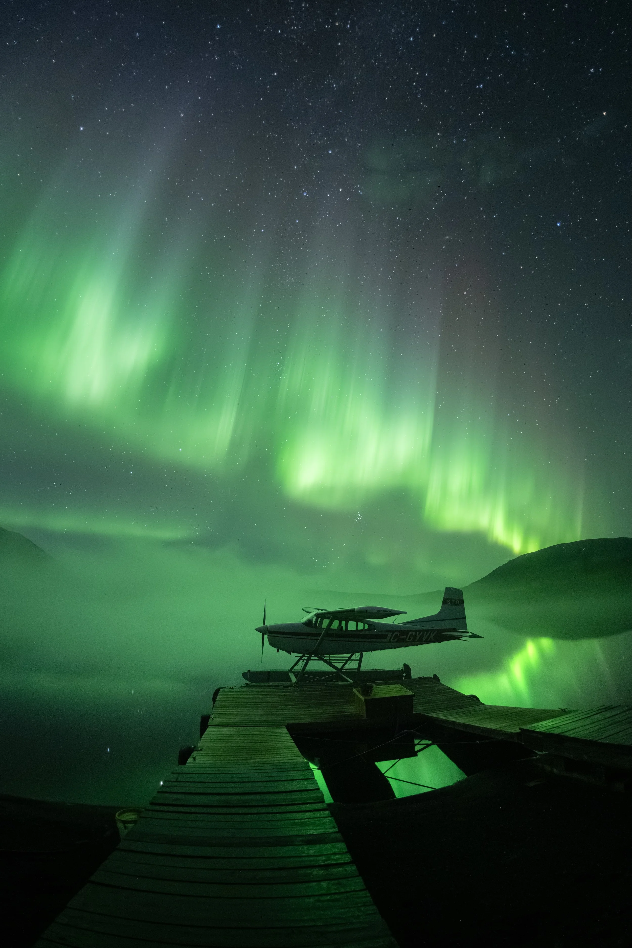 Vibrant display of Northern Lights dancing over a cessna 185 plane on Laslui Lake, at Spatsizi Lodge in the Spatsizi Plateau Wilderness Park, in Northern BC