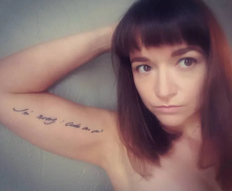 Photo of Jessica Morey-Collins with a line of Dickinson's handwriting tattooed on her arm. It reads, "I'm Nobody! Who are you?"