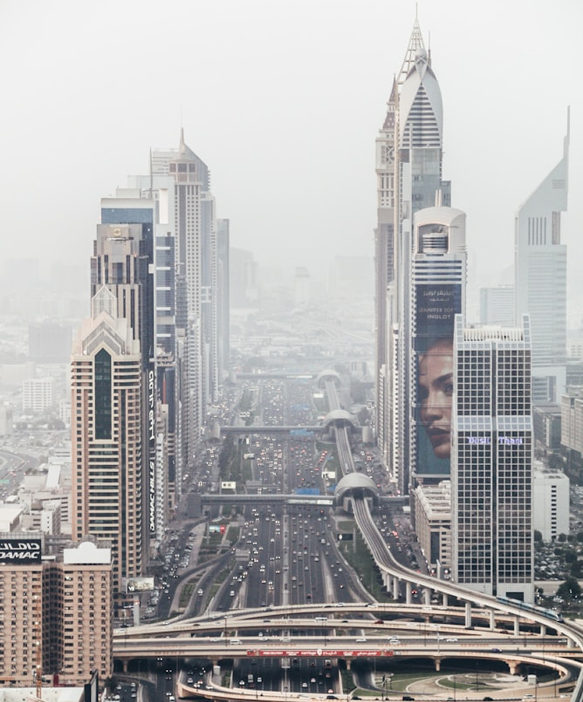 A cityscape featuring tall skyscrapers, with multiple highway roads and bridges in the foreground, under a hazy sky.