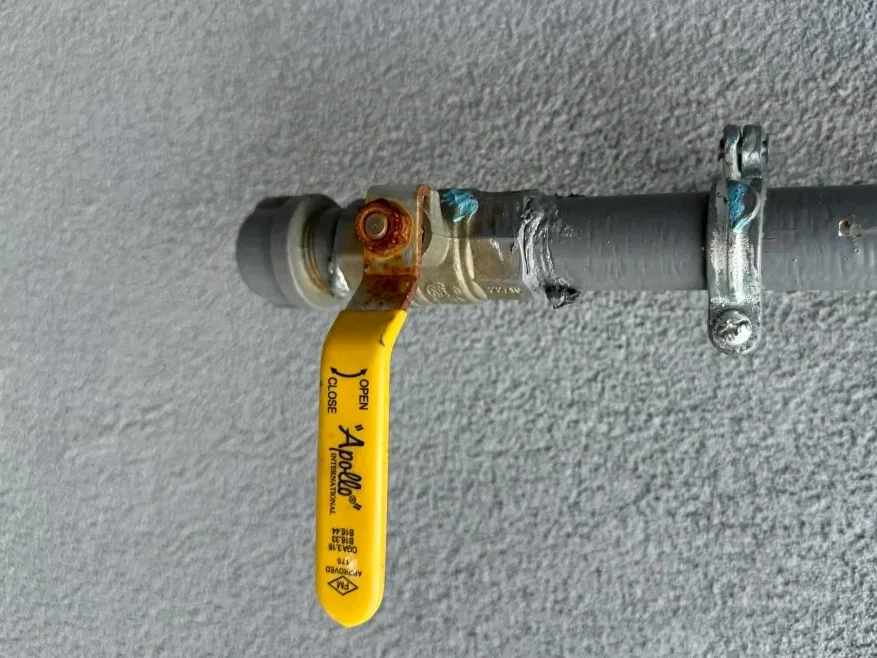 Gas line with a yellow shutoff valve handle on an exterior stucco wall