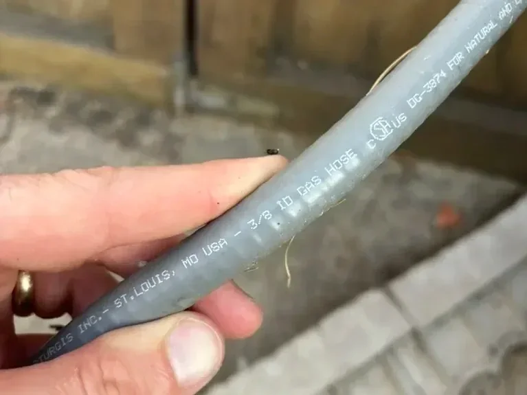 Hand holding a natural gas BBQ hose with the 3/8 inch size stamp visible