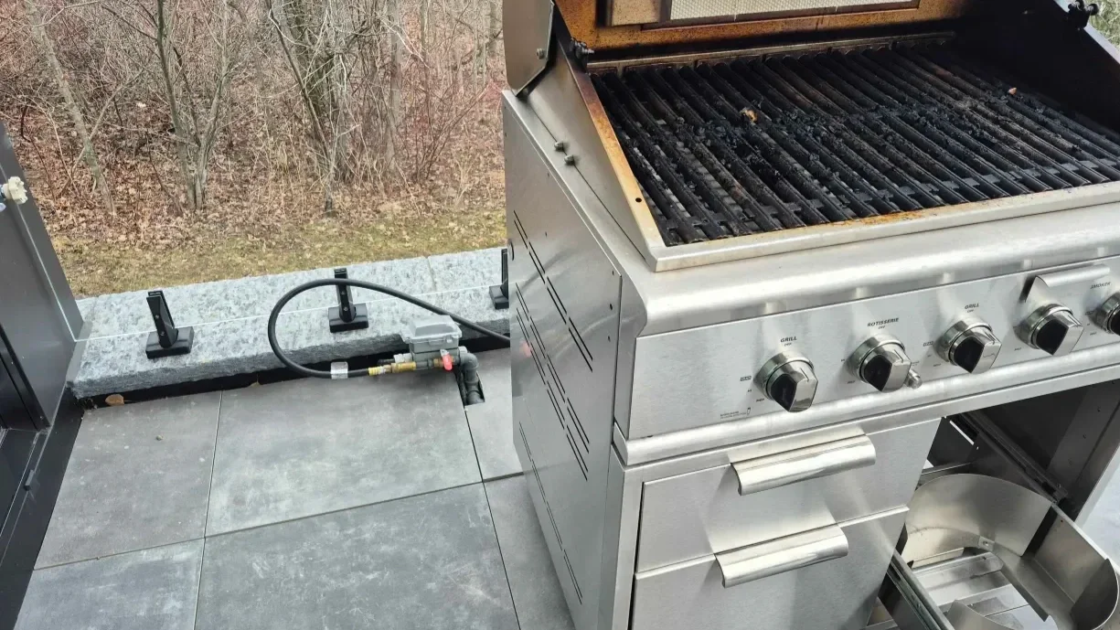 BBQ connected to a gas line on a patio, showing the hose running to the outdoor connection point