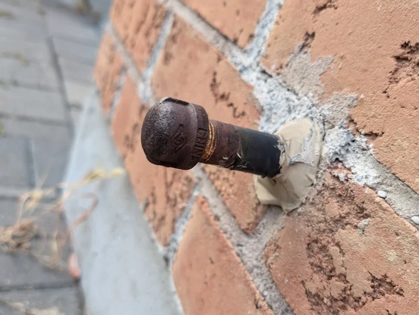 Capped gas line coming out of a brick wall with no shutoff valve