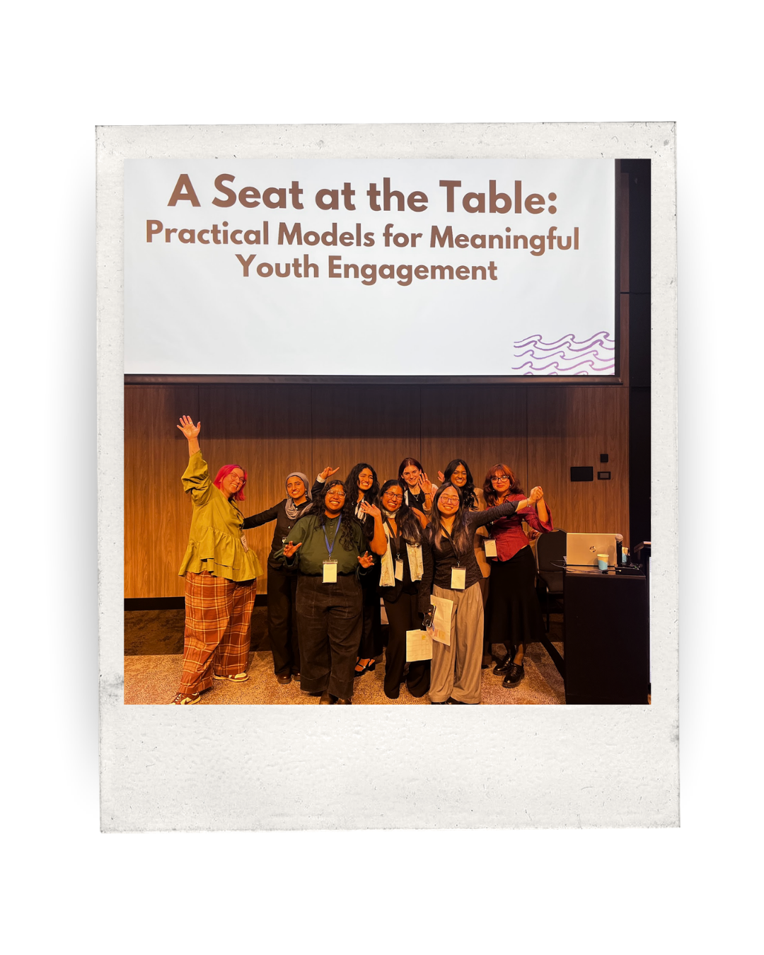 a group of young people posing beneath a power point thaat says 'a sat at the table: practical models for meaningful youth engagement'
