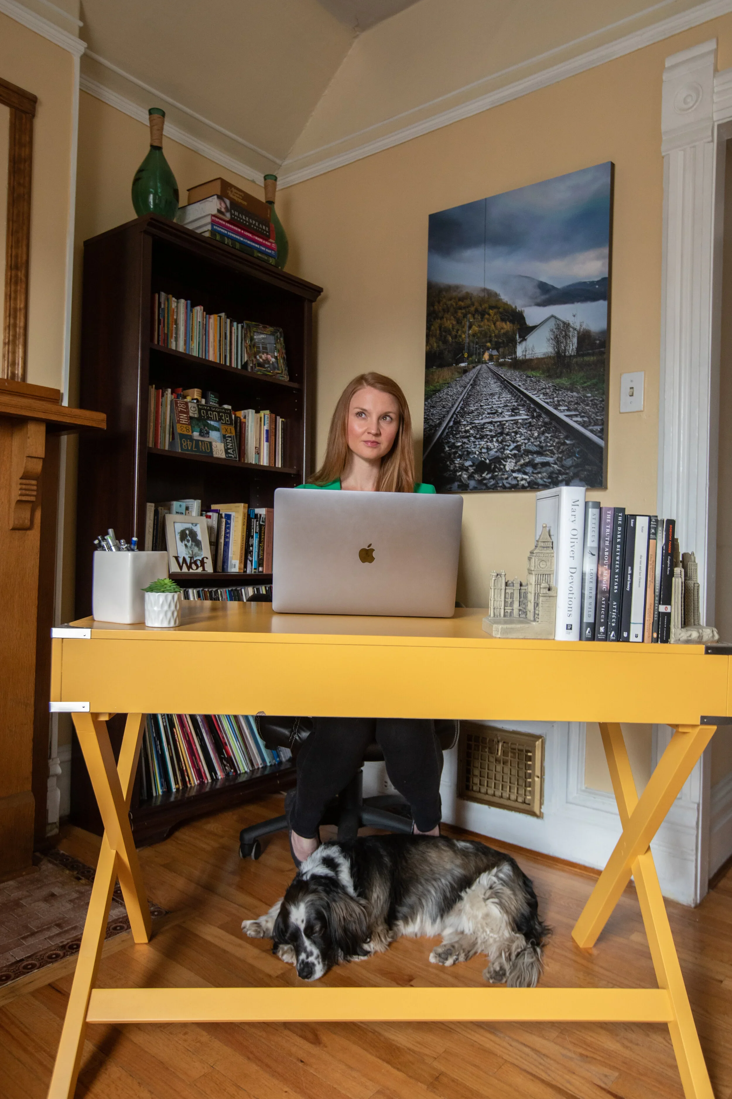 Chloe sits at a desk looking inspired, with a calm dog sleeping below.