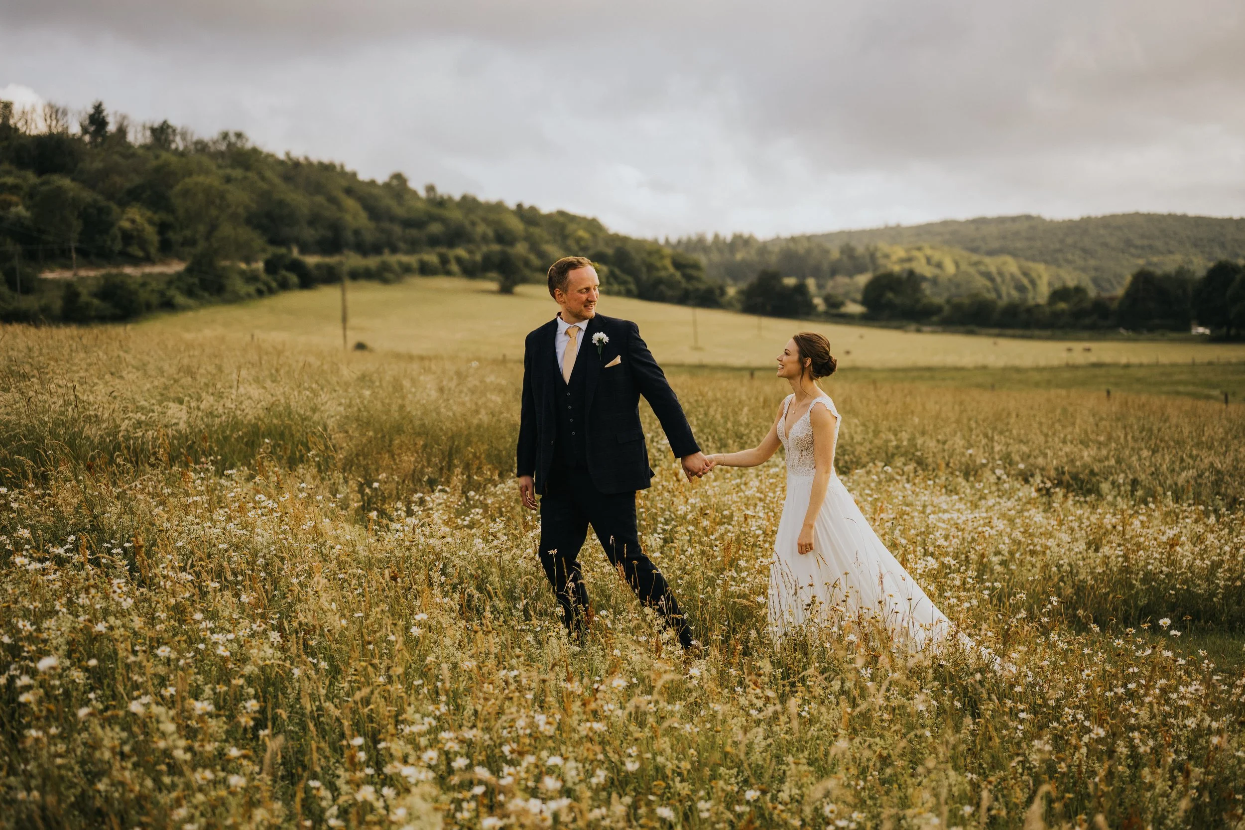 Groom leading bride through a feild of flowers at upwaltham barns
