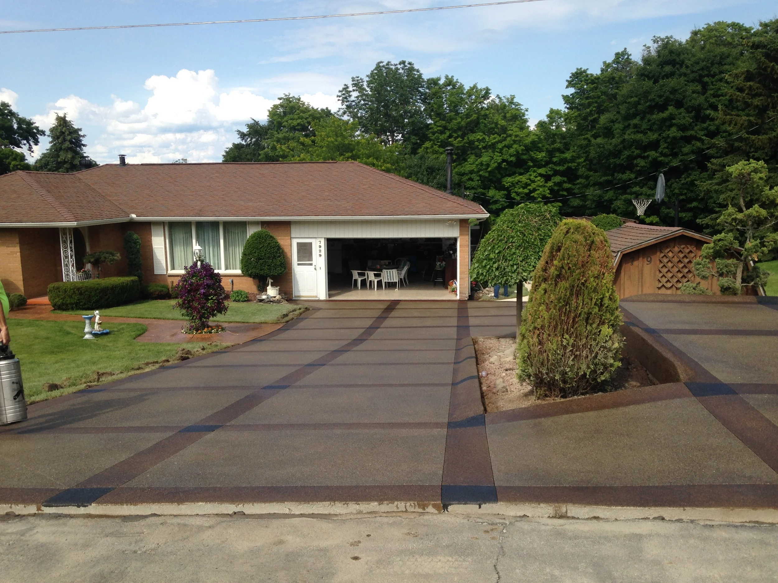 A large dark brown driveway with darker brown trip and dividing lines to make a grid. The driveway is a square with a small garden in the center.