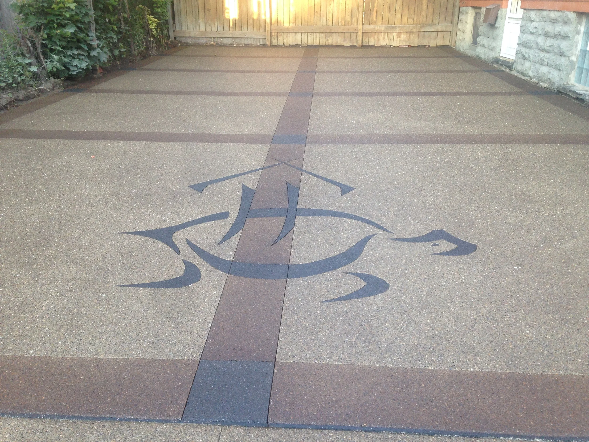 A black turtle design is stamped into the center of a light-colored concrete driveway. Dark brown lines split the driveway into a large grid.