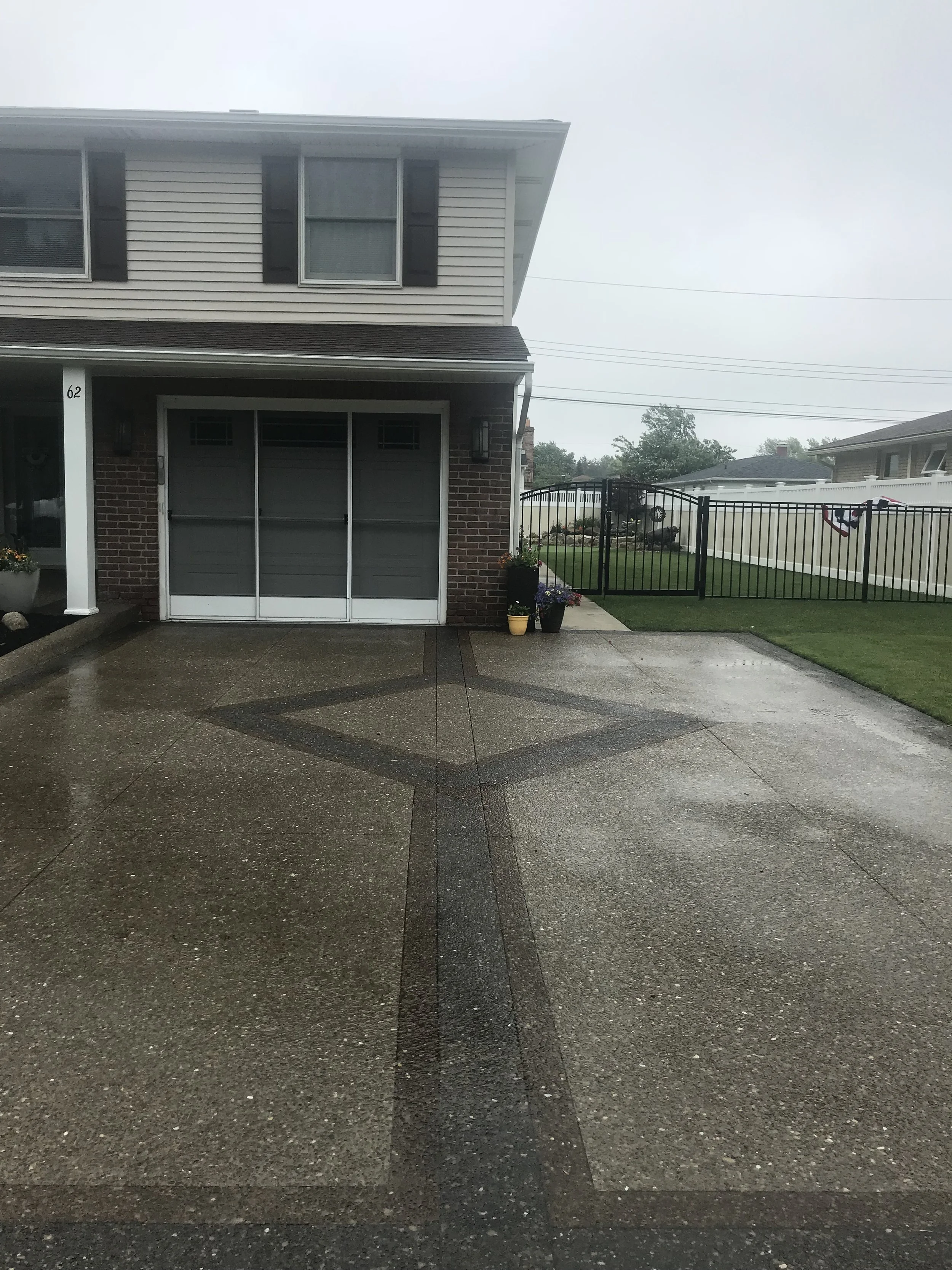 B&amp;W Custom Concrete Driveway. A light-colored driveway with a dark line through the center and a diamond in the center. It leads up to a built-in garage.
