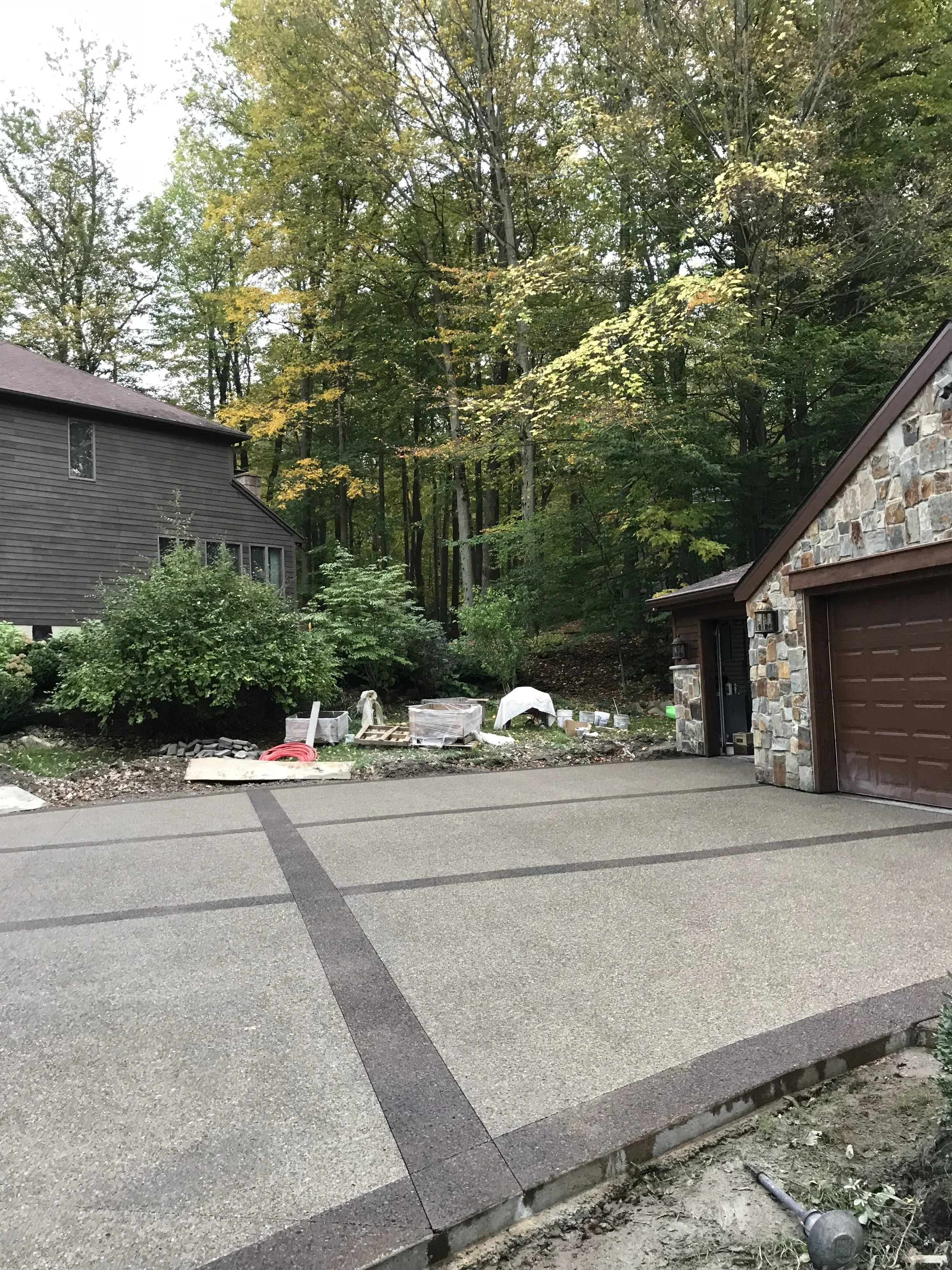 Custom built driveway. Light gray driveway with dark gray criss-cross pattern against a stone garage with woods behind it.