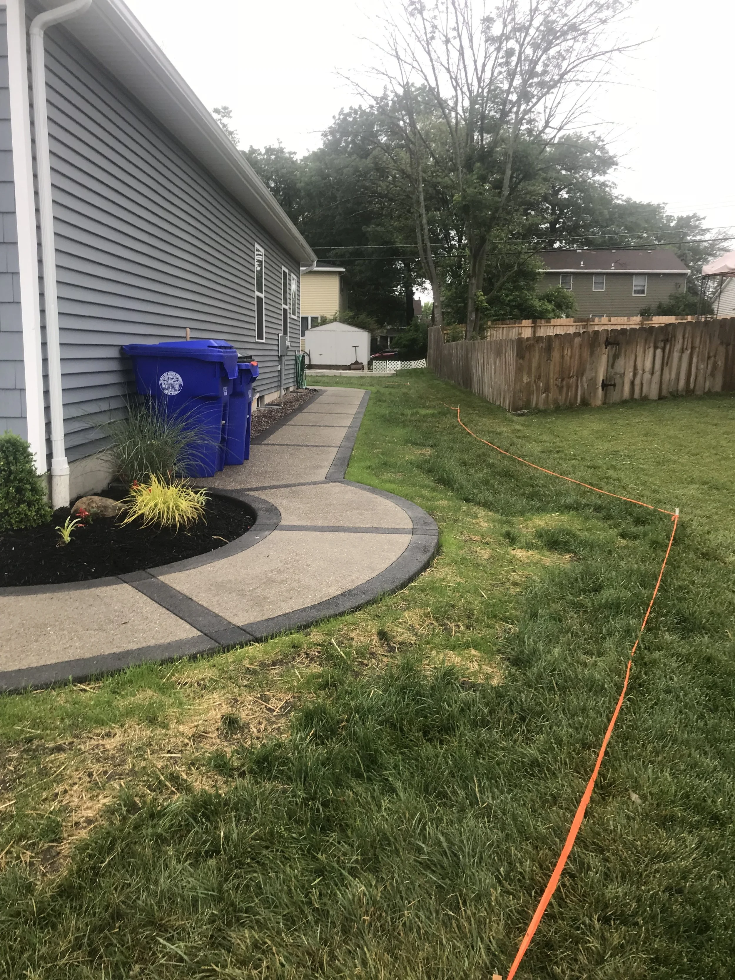 B&amp;W Custom Concrete Pathway in Buffalo NY. Curved, light-colored concrete walkway around the side of a house. It's divided into a grid pattern with dark concrete.
