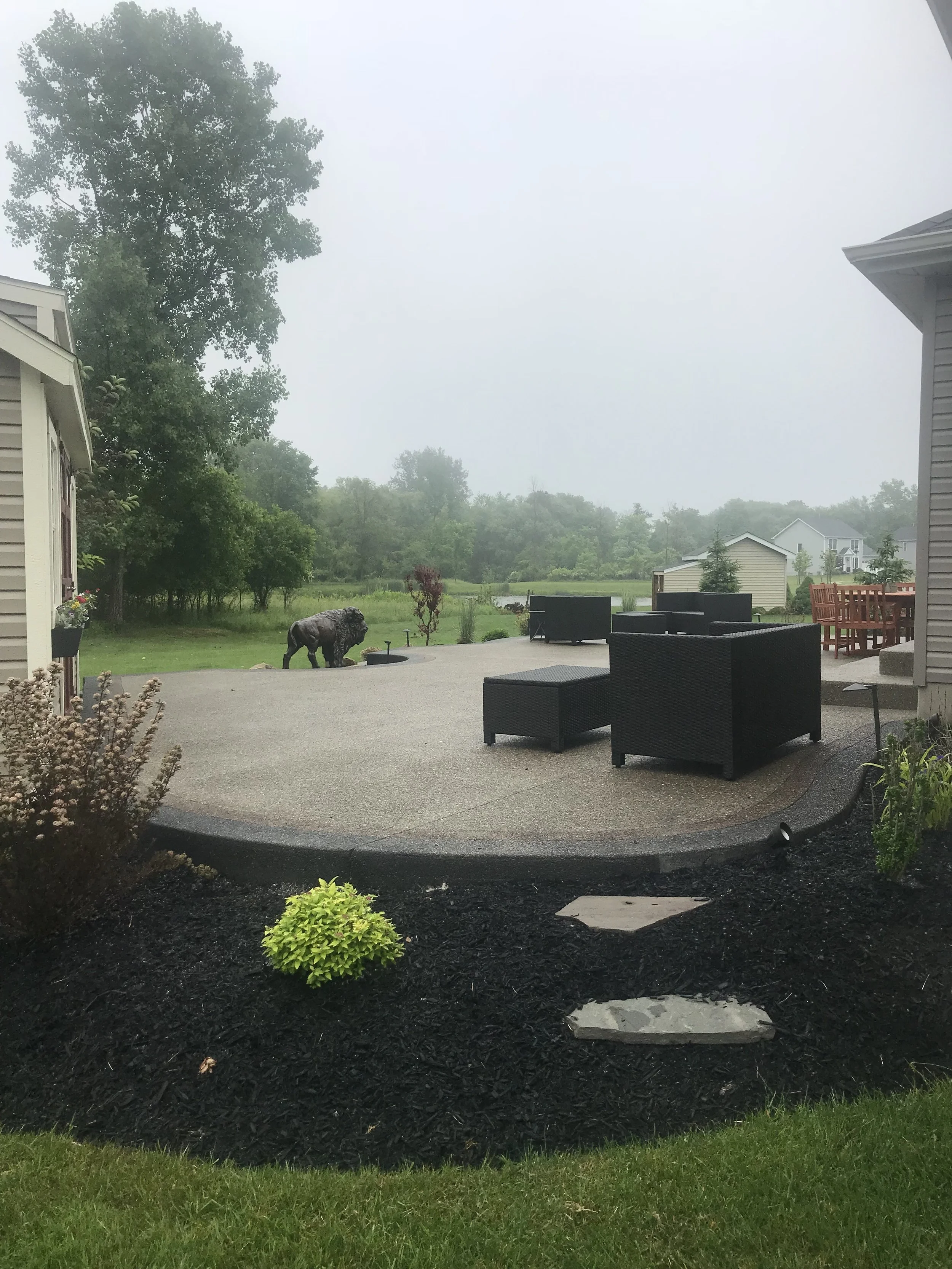 Custom Concrete Construction in Buffalo NY. A curved, light-colored concrete patio, surrounded by gardens. Patio furniture is setup.