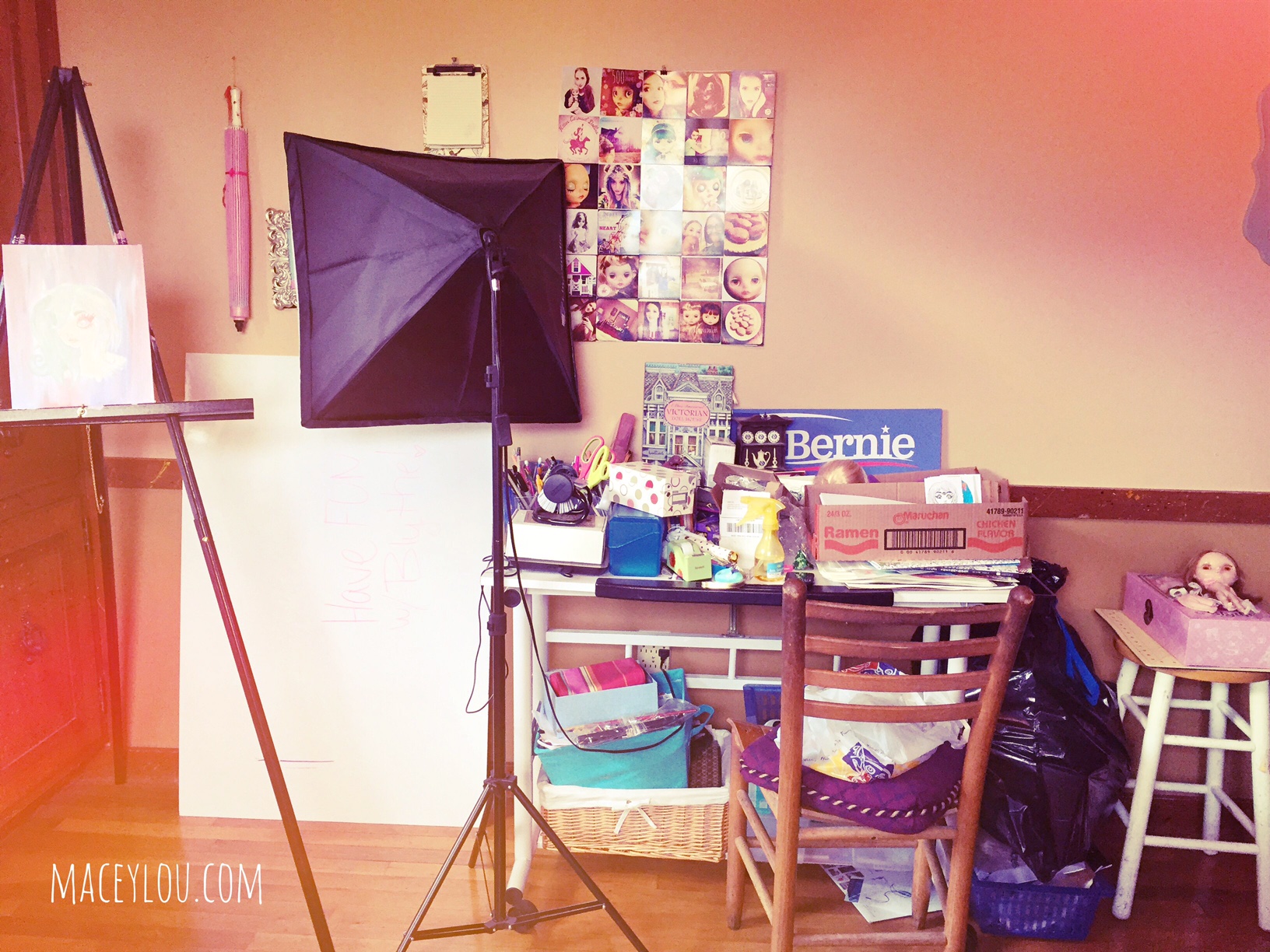 from left to right: my current painting, my dry erase board that needs a permanent home, one of my video lights, my photo collage, my clutter-filled table, and a chair and stool....