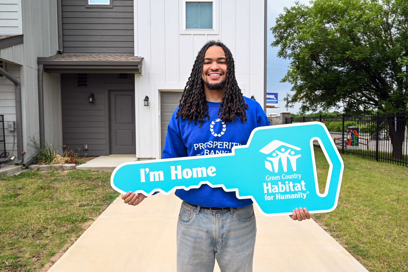 Young African American man standing in front of his new townhome holding an oversized Green Country Habitat for Humanity key