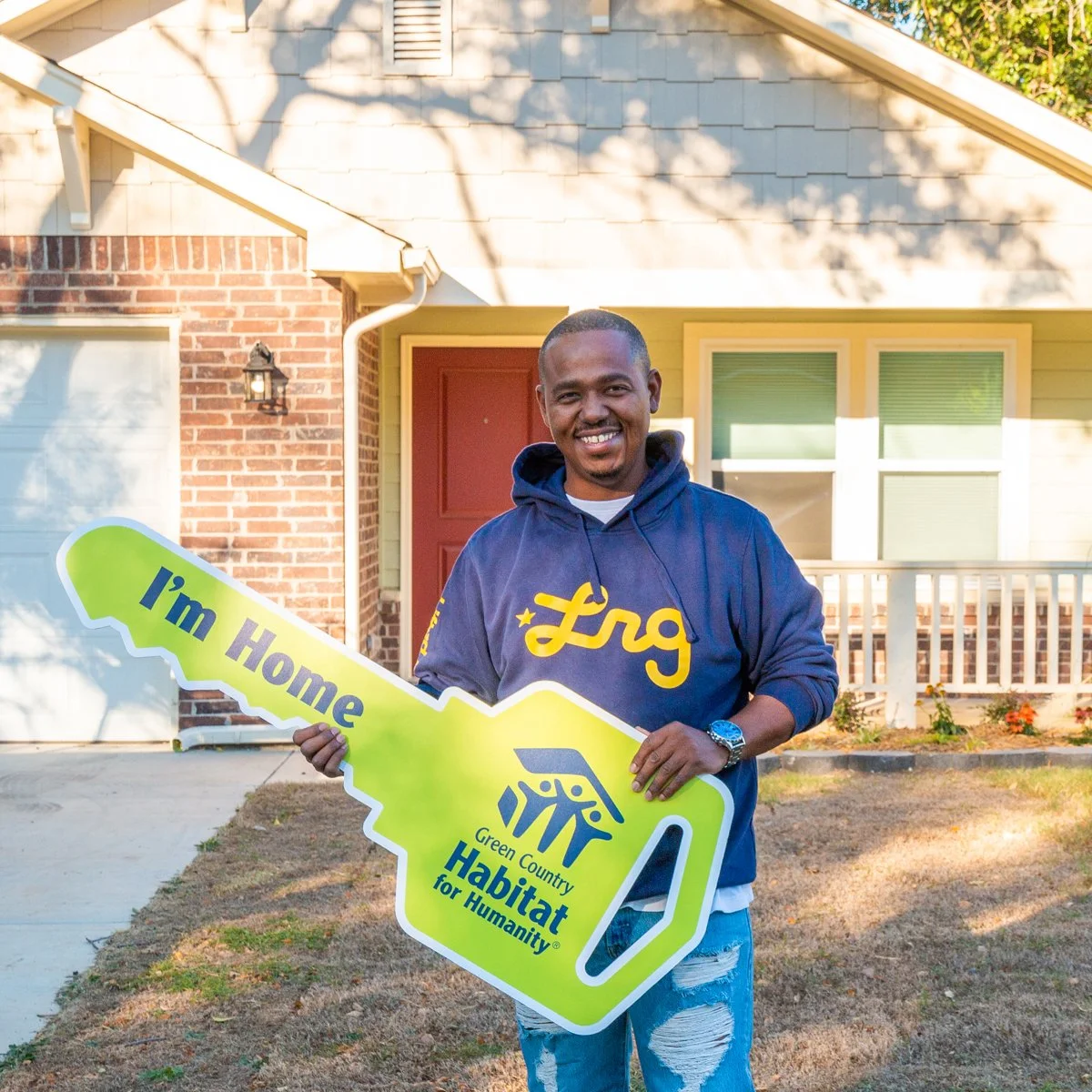 photo of new homebuyer holding oversized key in front of his new home