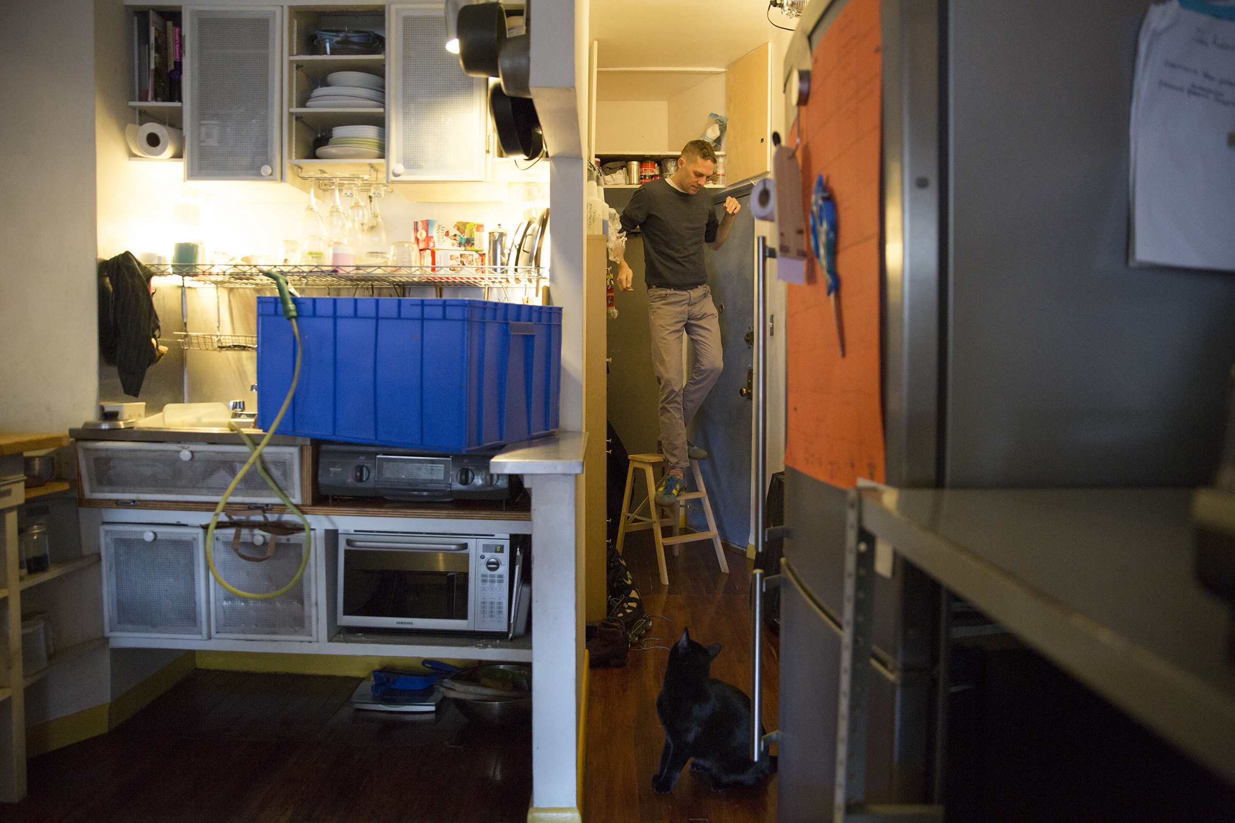 A blue storage bin doubles as a washing station, set up on the sink where Anselm has custom fit a rubber hose to fill it. He is in the back, getting supplies stored in a nook above his daughter’s room.