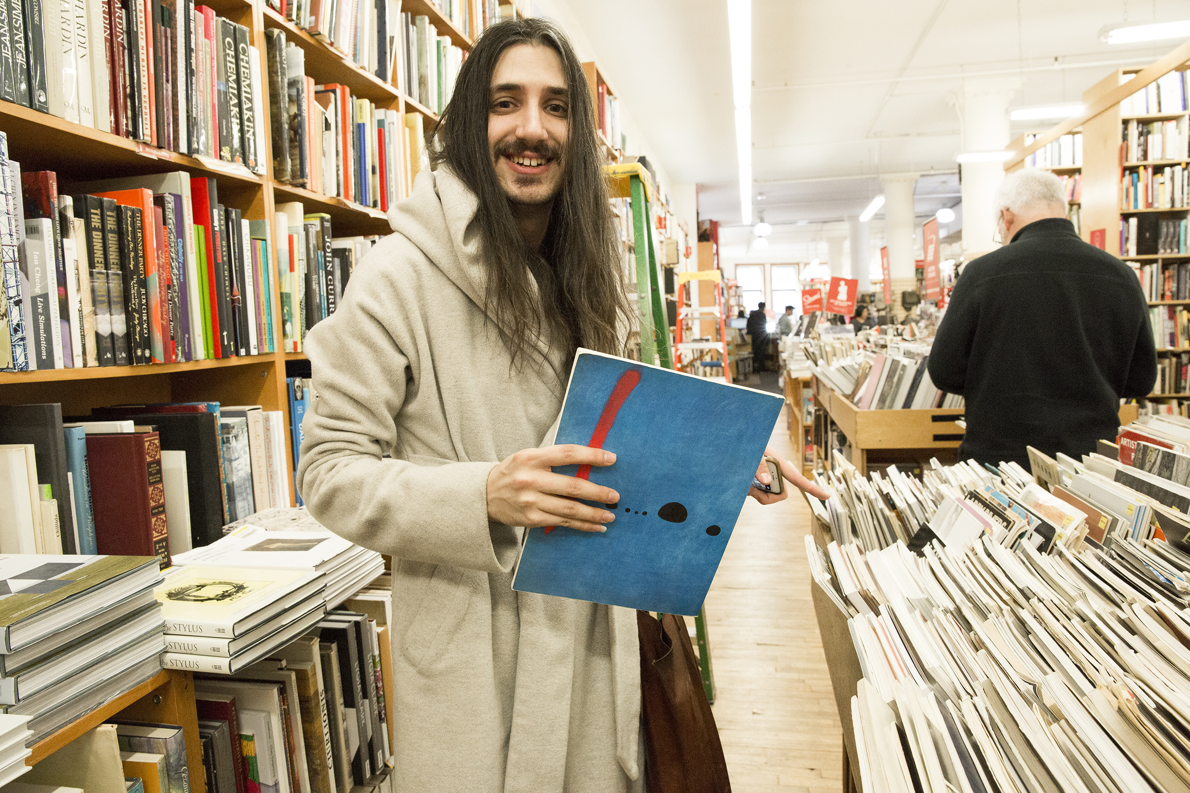 Aaron browses the used book section. The Joan Miró “Blue” painting on back cover of the book they’re holding happens to be a poster in their room.