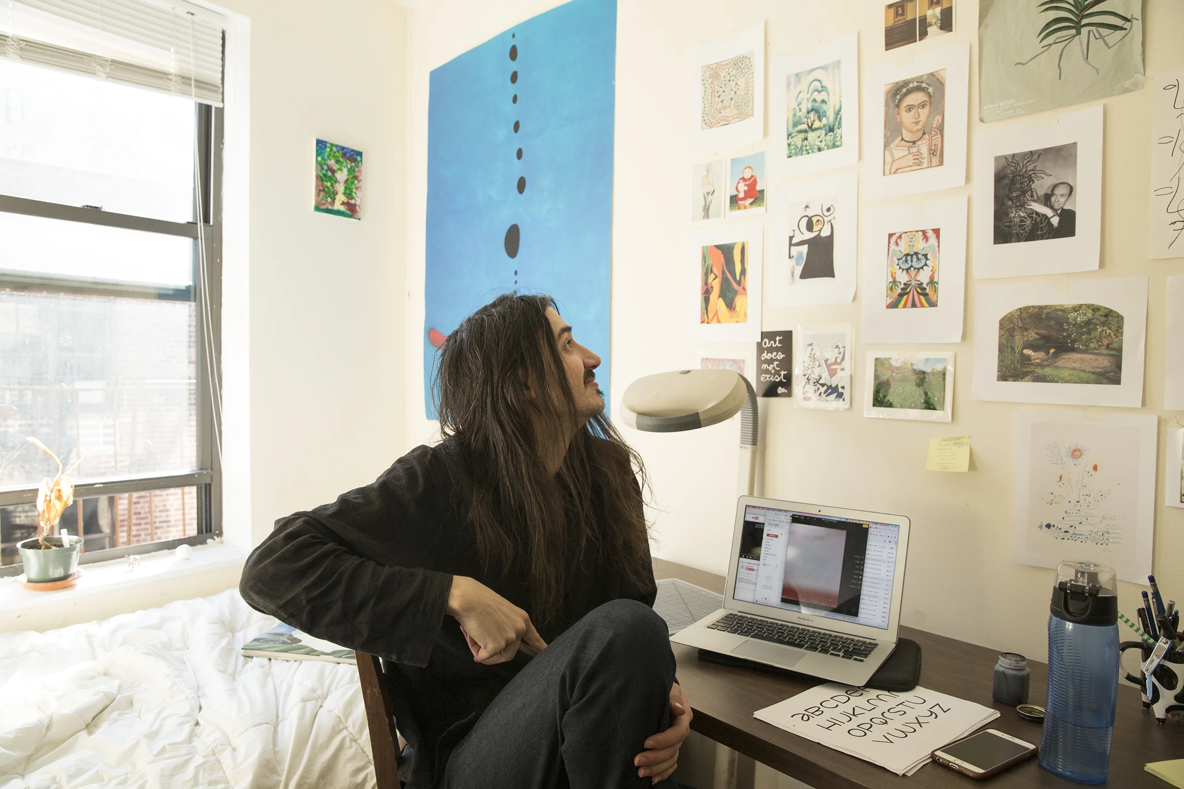  Aaron sits in their room at home in the West Village where they share a small apartment with a roommate. The wall is covered in artworks and ephemera that inspire them or relate to a project they’re working on. Note the Joan Miró “Blue” poster on th
