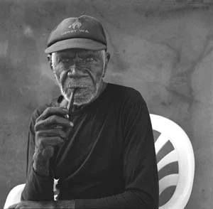 11 Ngarra, Andinyin/Kitja Artist, c.1920 to 2008: HENRY F. SKERRITT Ngarra at home in Derby, 2002. This photograph was taken by Ngarra's long-time friend and facilitator Kevin Shaw, and appears in Shaw's publication Mates: Images and Stories from the Kimberley, Australian Scholarly Publishing, Melbourne 2002. Ngarra approved of his photographic image being used after his death