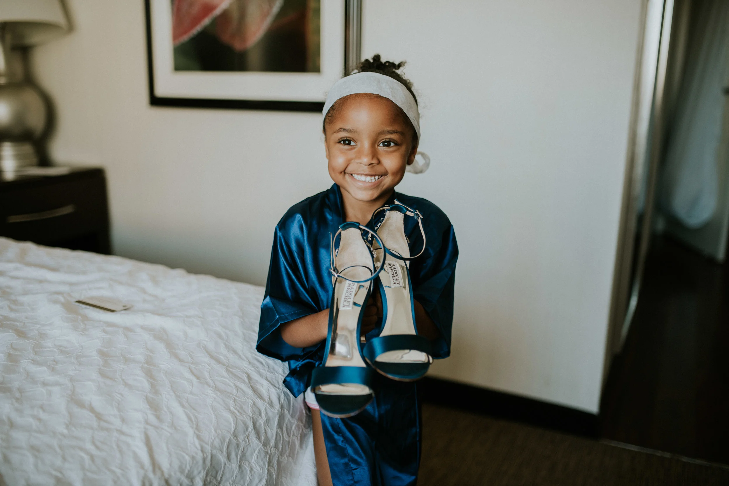 Flower girl smiling while holding bride's navy Badgley Mischka designer heels