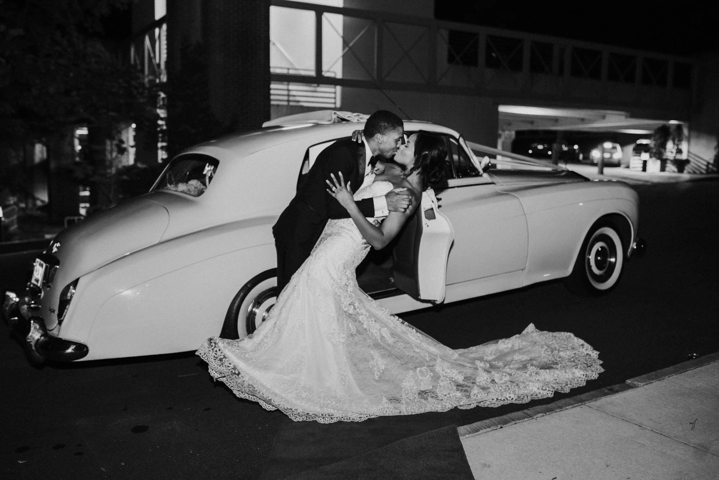 Bride and groom kiss in front of vintage car