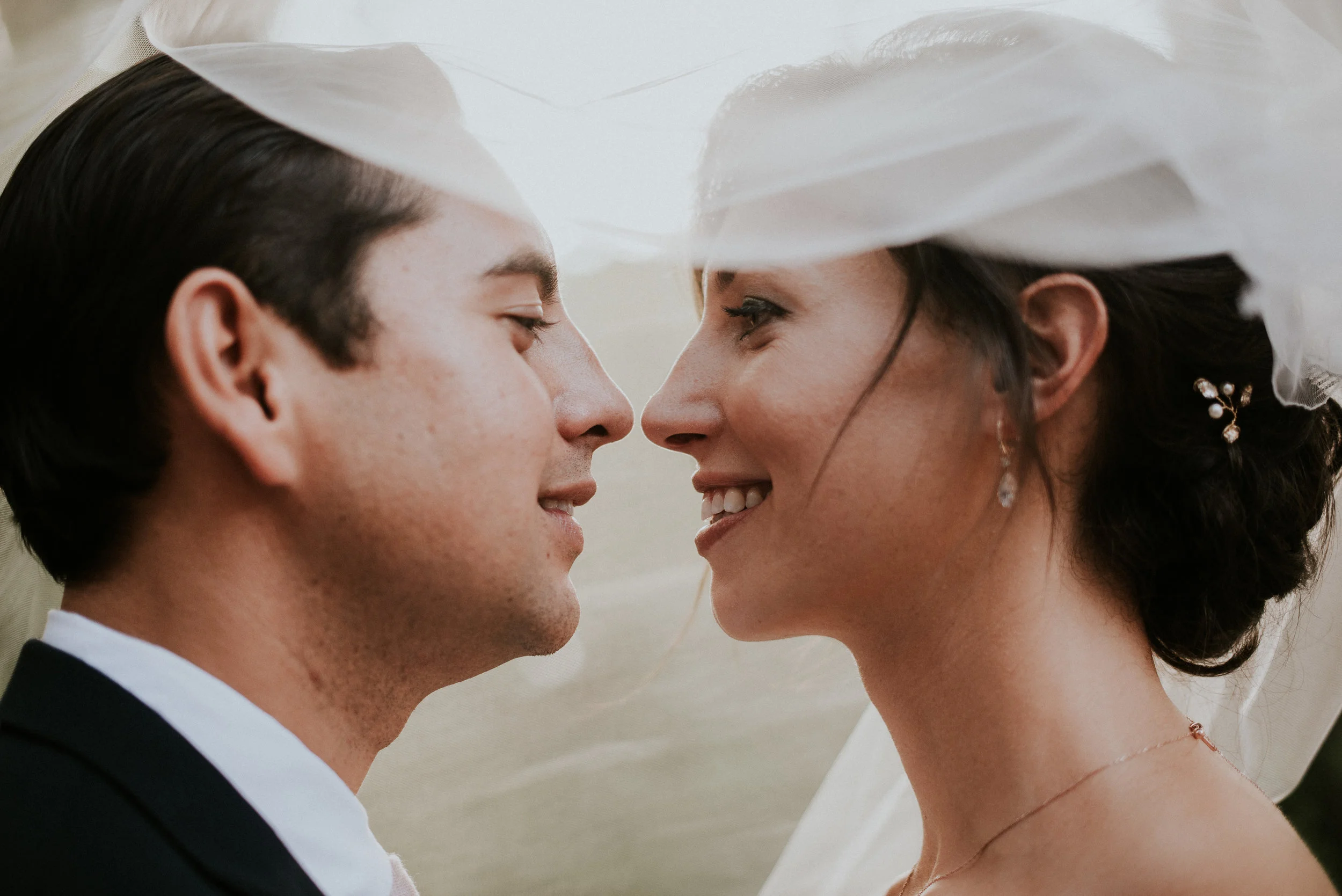 Bride and groom smiling underneath veil