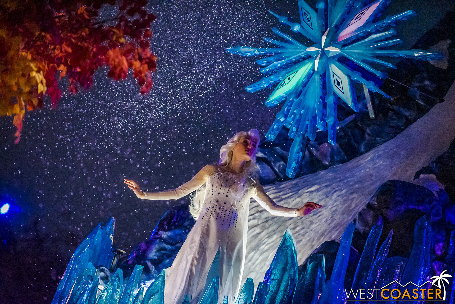  Elsa strikes a dramatic figure, high on the icy and shimmering mountaintop, under an iconic snowflake featuring symbols of the four elements as shown in the movie. 