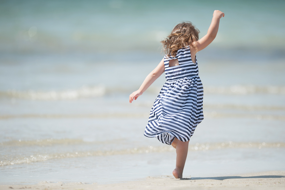 Carefree little girl dancing in the waves during family portrait