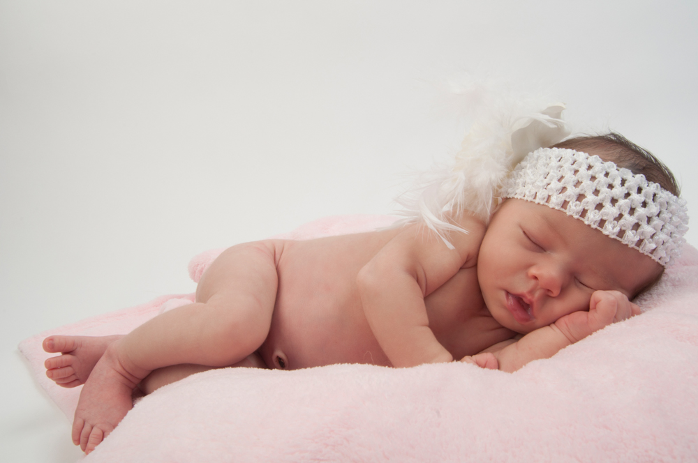 Beautiful newborn baby girl laying on a pink blanket with a feat