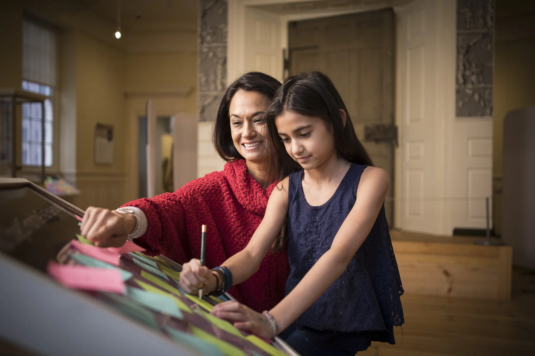 Mother helping instruct a young child in writing on an interactive display.