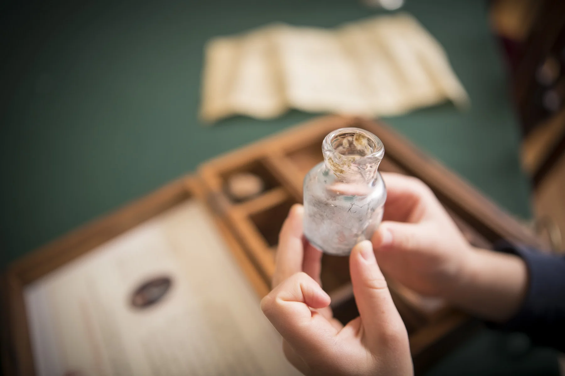 Close up of a child's hands holding an inkwell from a box of wooden artifacts.