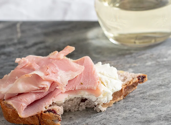 Cranberry Walnut Round Bread with Rosemary Ham and Goat Cheese with a bite taken out of it.