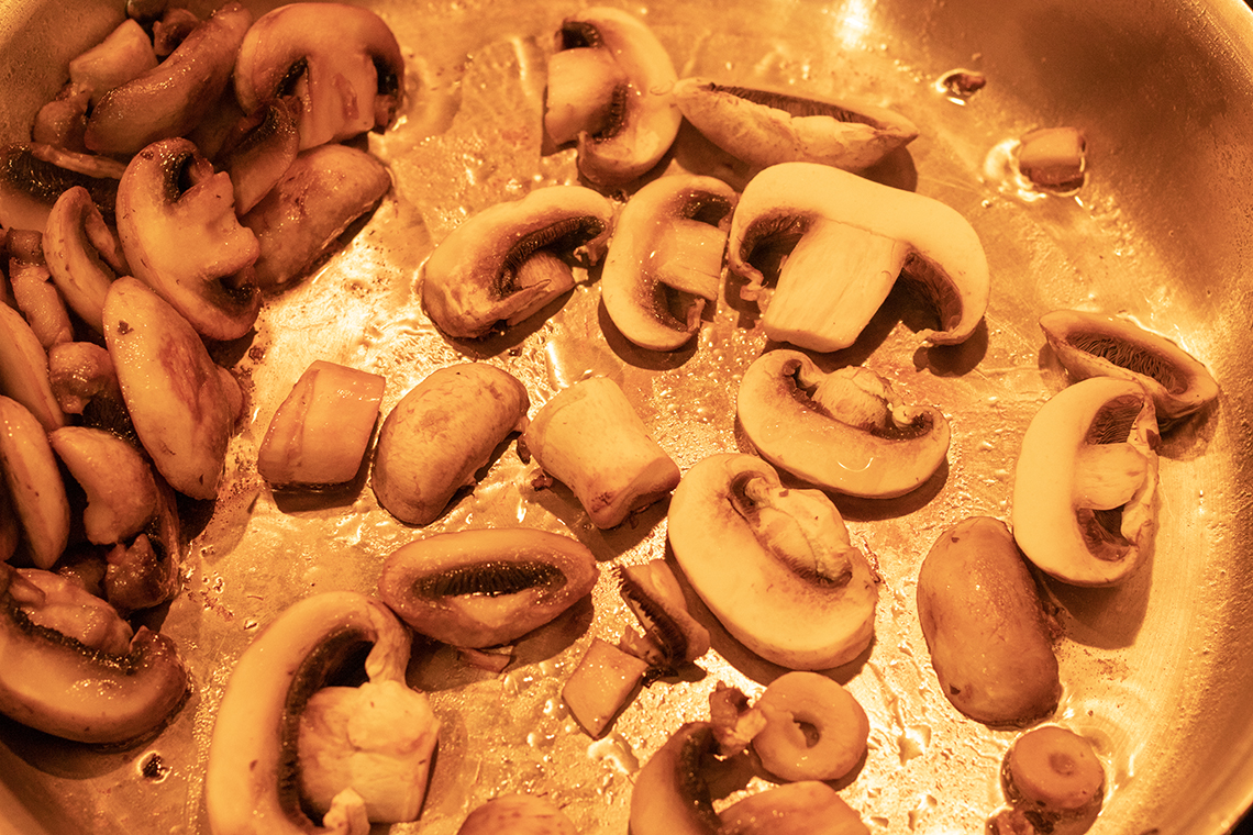 Mushrooms being sautéed in a skillet in batches. Each batch is pushed to the side of the skillet while the next batch is browning.