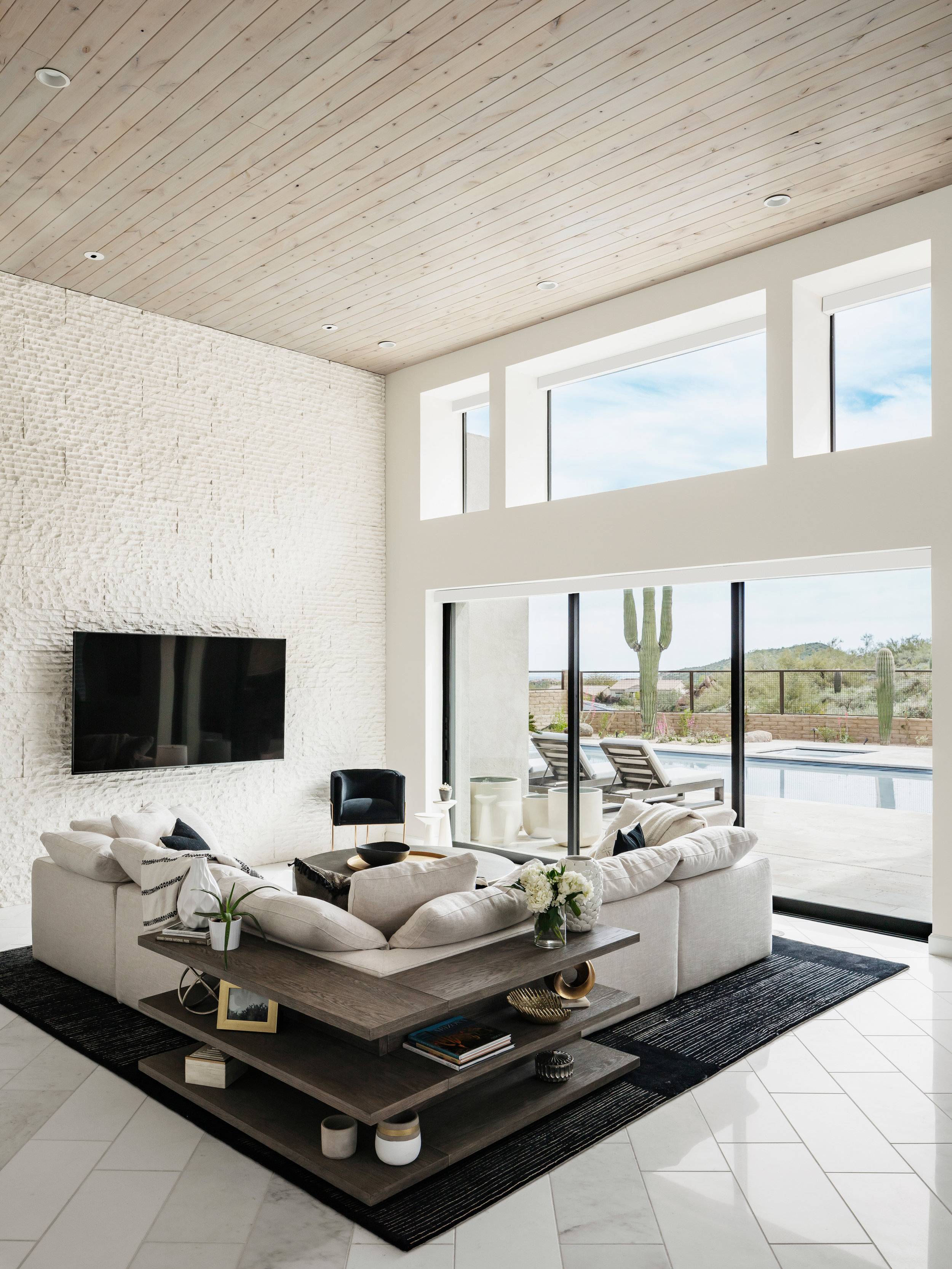 This neutral palette is grounded by a dark black rug to allow balance between the high ceilings, bright open windows and the living space. A storage unit cradles the spacious sectional to create a border to the space and allow for some unique access