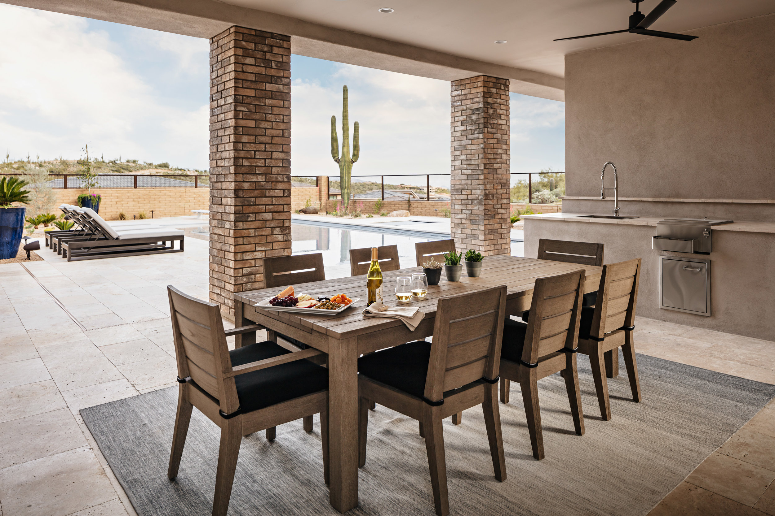 A neutral ombre rug pairs well with the sleek teakwood dining table and chairs. Highlighting the natural tones seen in the scenery around, makes for a seamless patio design. Image: Roehner + Ryan