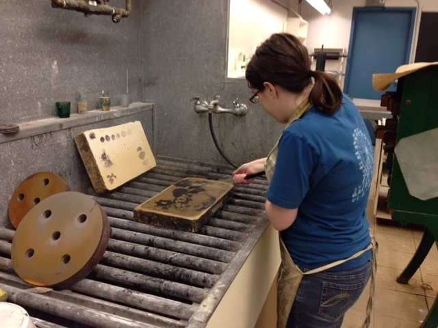  Here I use a hose to force a water jet to remove the excess grease from the stone, leaving only the black marks coated with grease. The giant wheels to the side are used to grind old images off of lithography stones so that they can be reused. It is