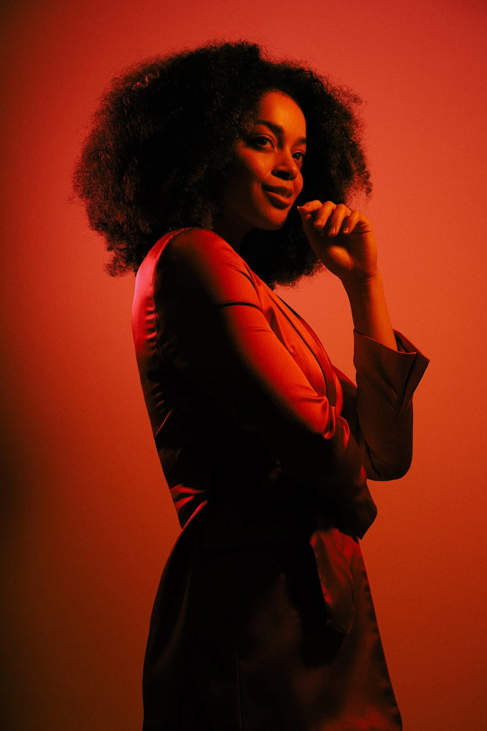 Mid-length portrait of a woman in orange lighting with a slight, knowing smile