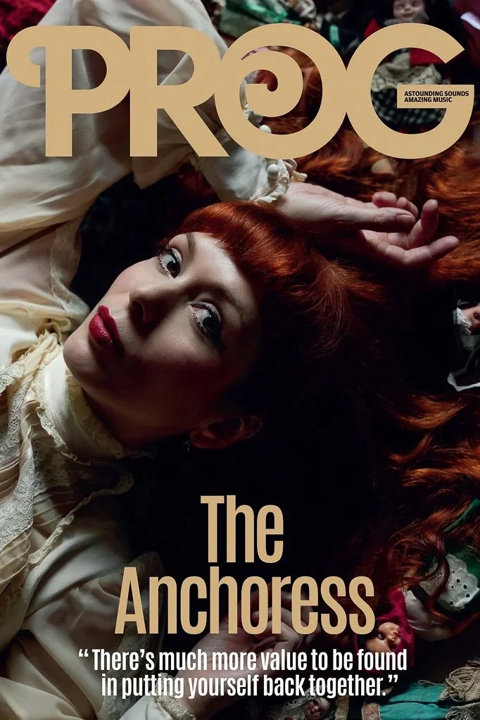 Cover of Prog magazine featuring a woman with red hair lying down, gazing at the camera, wearing a vintage cream-colored dress, surrounded by toys and objects, with the text "The Anchoress" and a quote about value and unity.