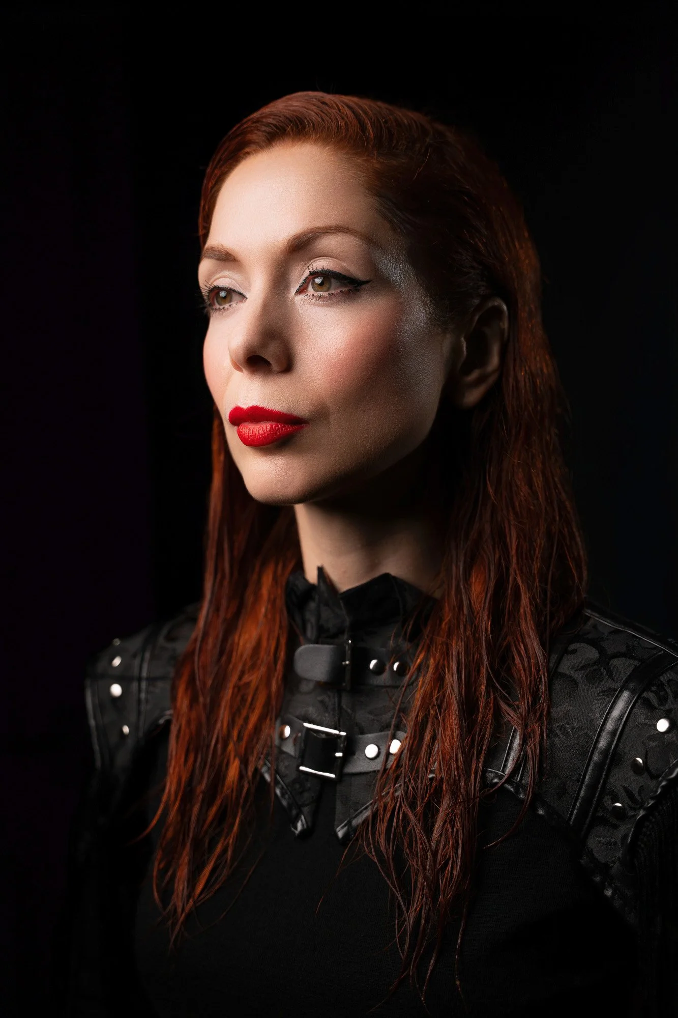 Close-up portrait of The Anchoress (Catherine Anne Davies) against a black background with an armour-like styling aesthetic