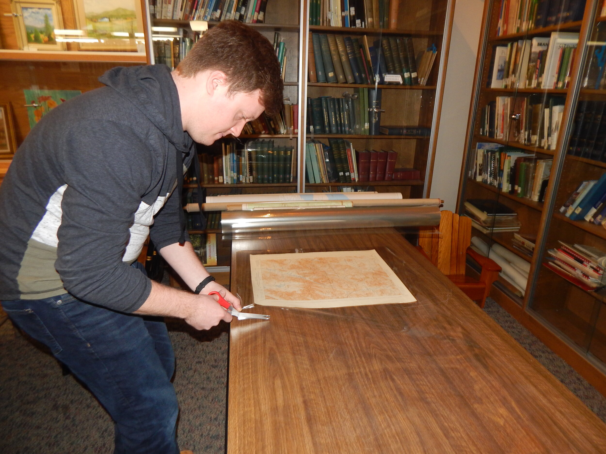    Conor cuts mylar to the size of a map so it will be preserved and protected.  