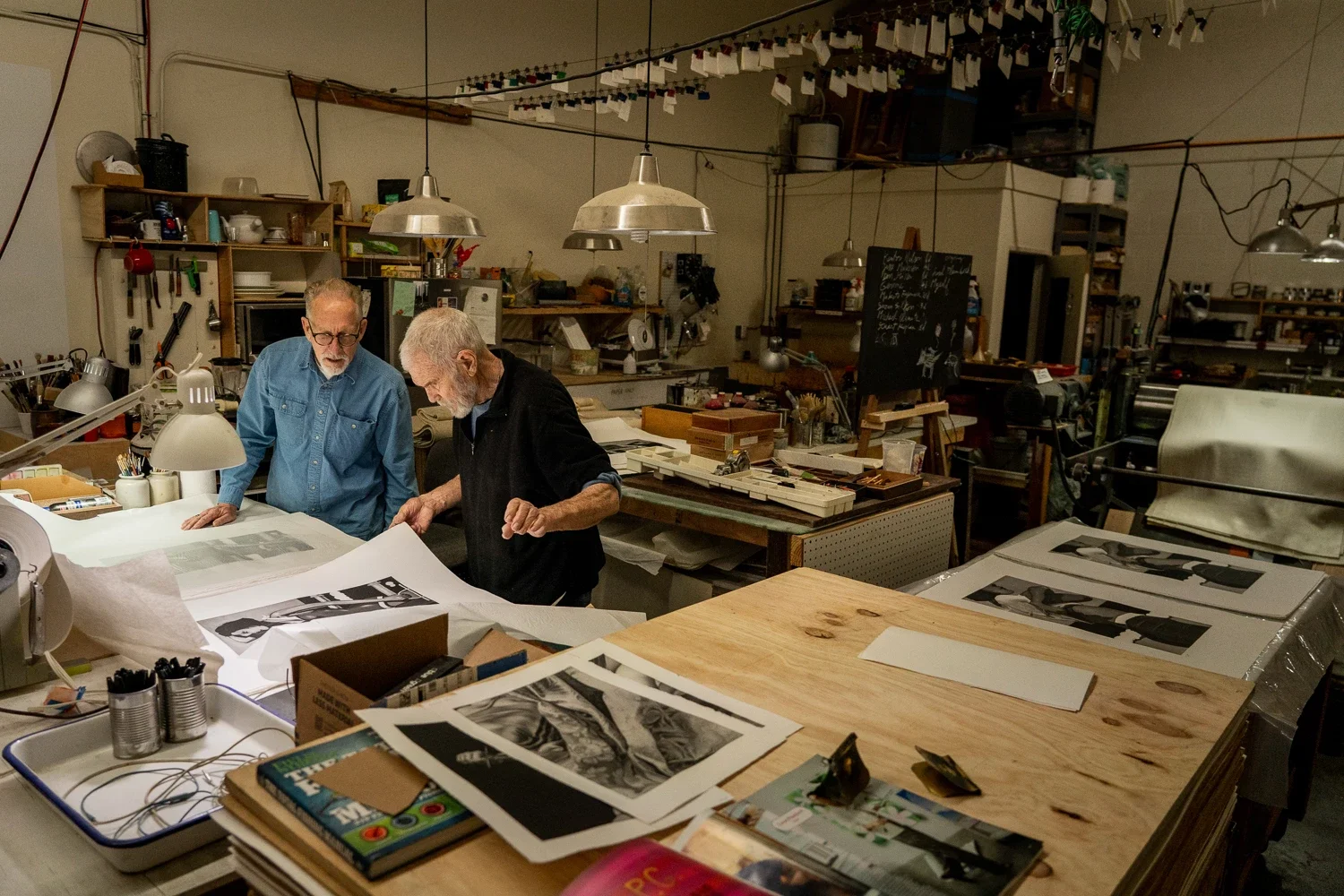 Artist Kenton Nelson and Master Printer Pascal Giraudon working together in a press print studio surrounded by prints and printing tools in the background