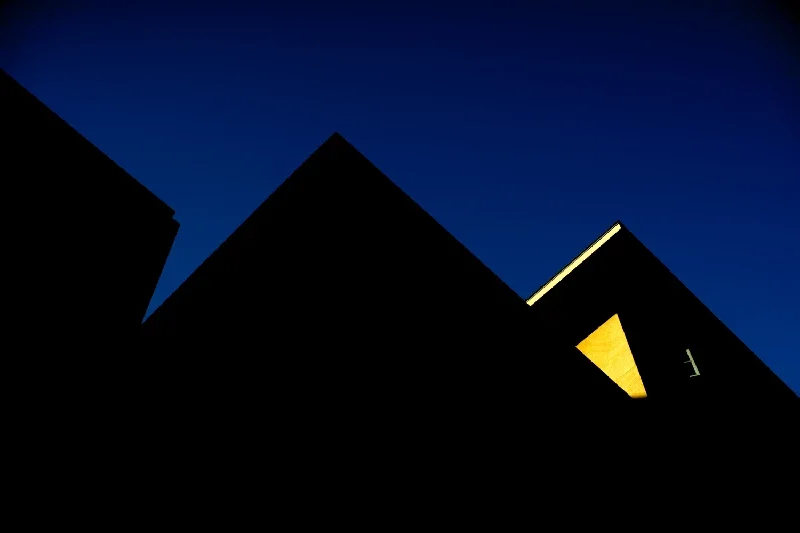 Silhouetted modern buildings against a dark evening sky, with faint illuminated edges.