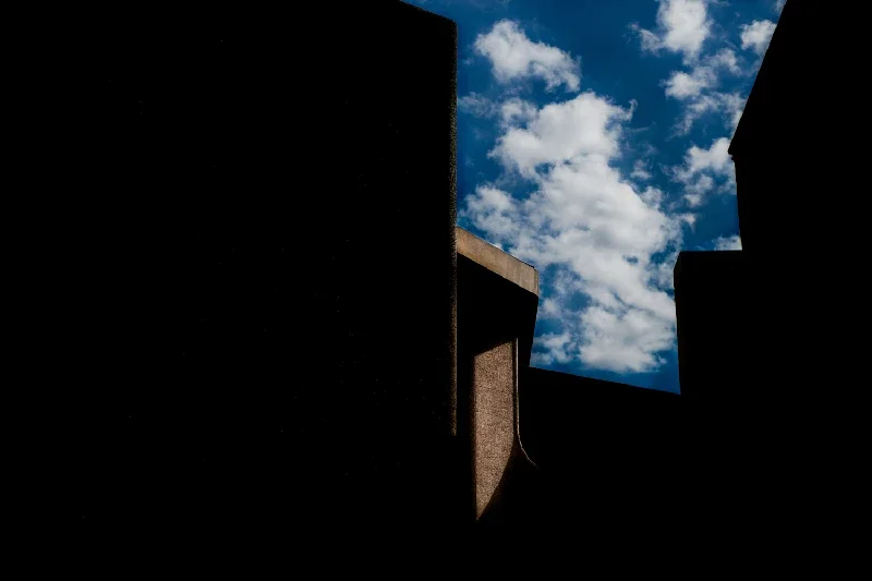 Silhouettes of buildings with a bright blue sky and scattered white clouds in the background.