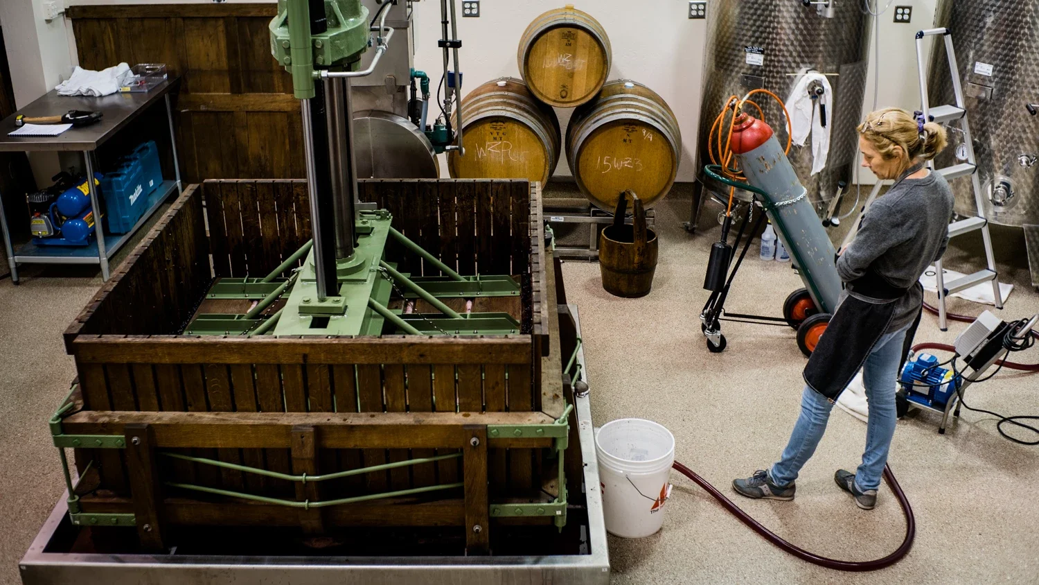 Cindy, the coowner of wenzlau winery waits as the french wine press is extracting the grape wine out of the harvested grapes in the winery